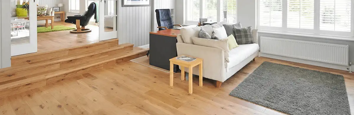 A modern living room with professionally installed laminate flooring, a beige sofa, a small side table, a gray rug, and large windows with white shutters in Boise, ID